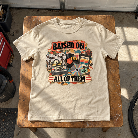 Cream vintage t-shirt on wooden table with printed Raised On All Of Them music design