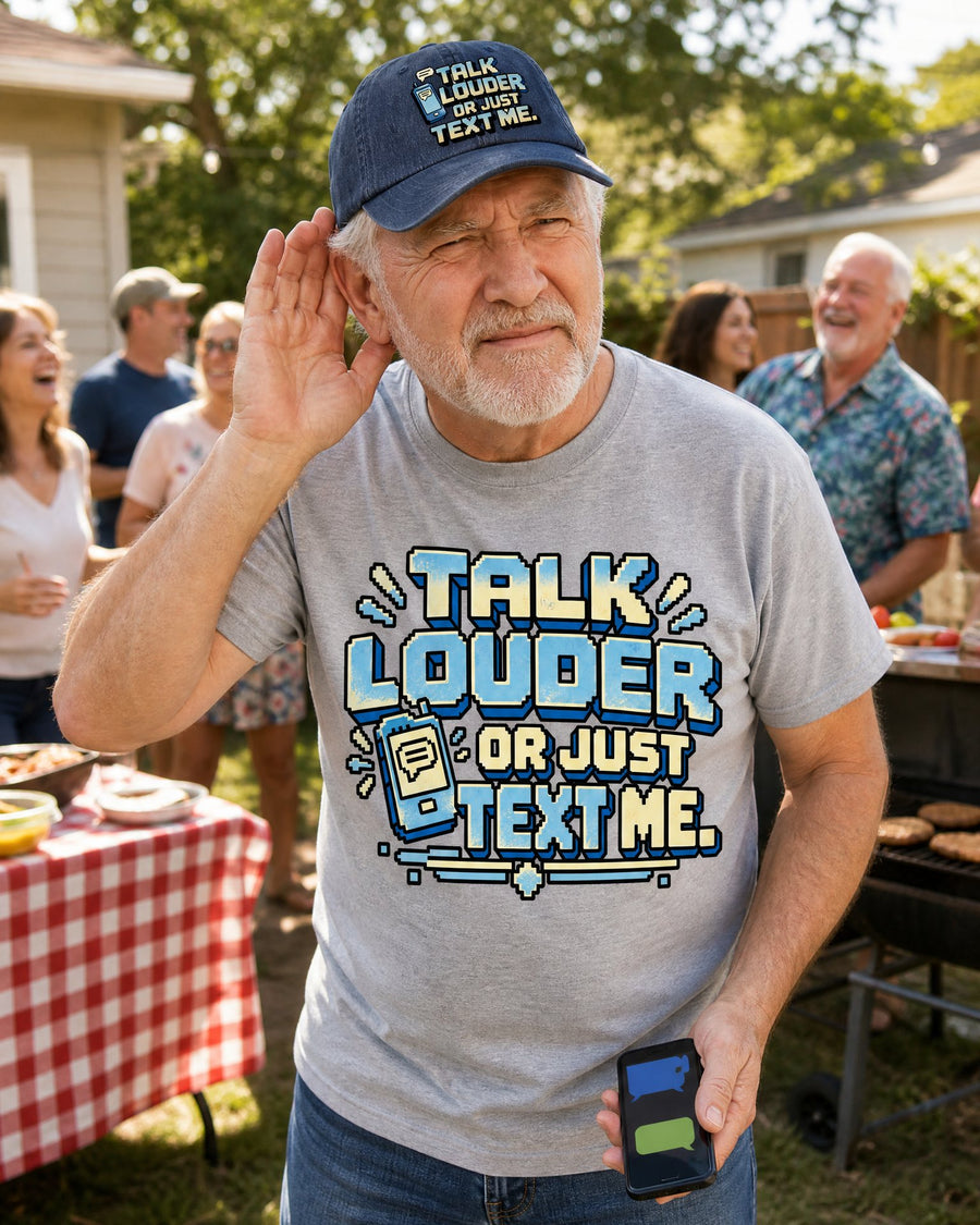 Man in the Talk Louder Or Just Text Me sport grey tee and navy cap cupping his ear at a family barbecue