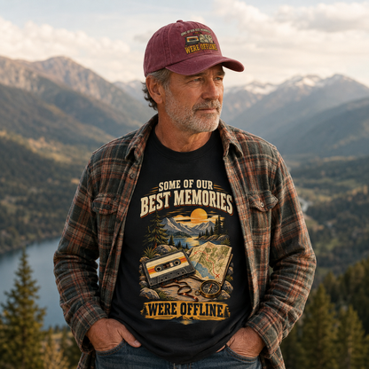A man wearing a maroon baseball cap, a brown and beige plaid flannel shirt, and a black graphic t-shirt with a mountain and cassette tape design, standing in front of a scenic mountain landscape.