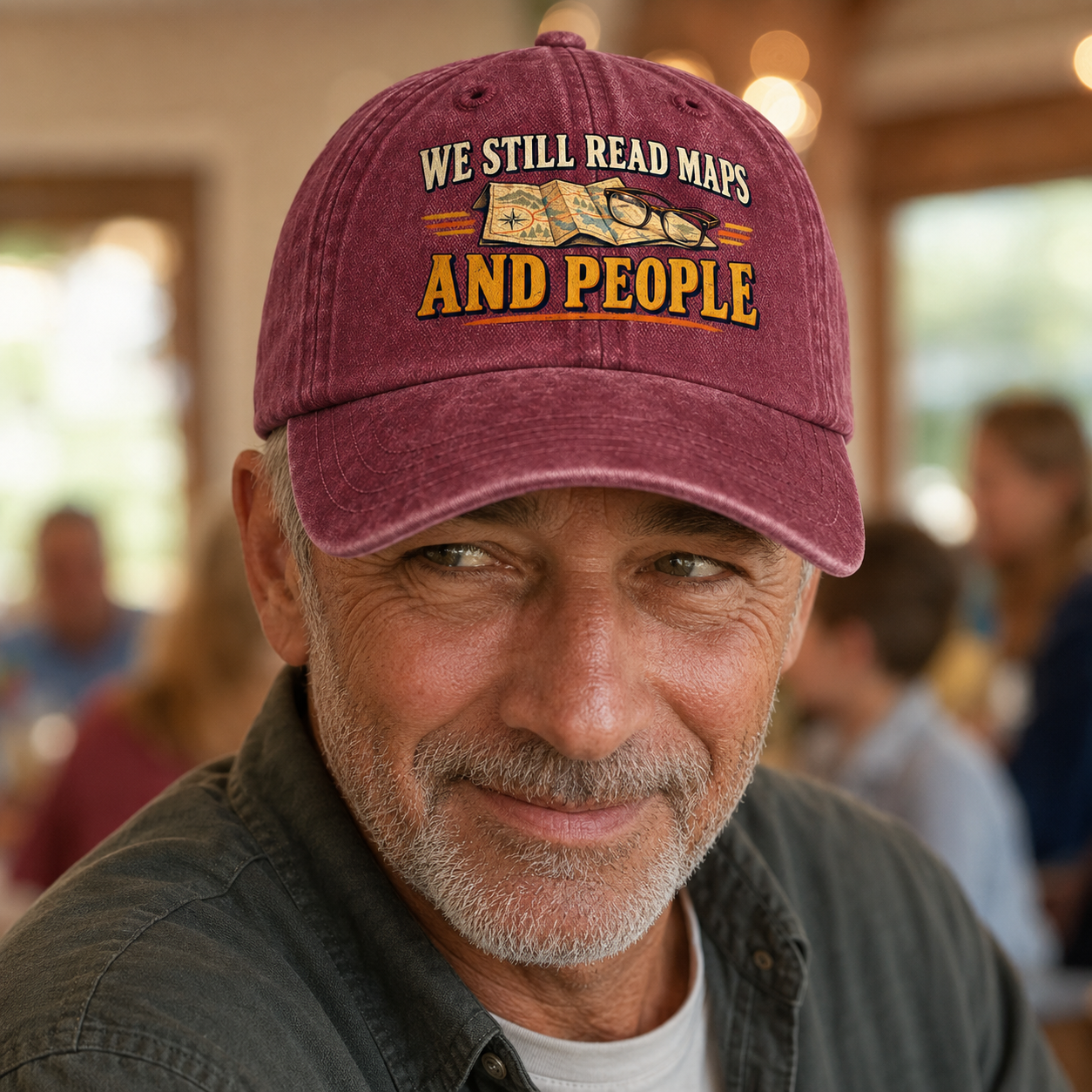 believable older man around 62 with weathered skin, gray stubble, and deep smile lines wearing the "We Still Read Maps And People" vintage washed cap at a family gathering, catching a silent signal across the room