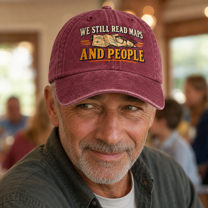 believable older man around 62 with weathered skin, gray stubble, and deep smile lines wearing the "We Still Read Maps And People" vintage washed cap at a family gathering, catching a silent signal across the room