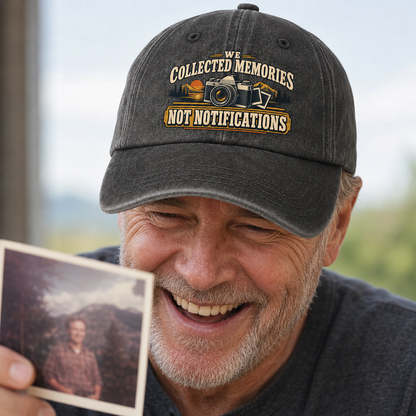 A smiling man wearing a dark gray baseball cap with an embroidered graphic that reads 'WE COLLECTED MEMORIES NOT NOTIFICATIONS' with a camera and photo frame motif. He is holding a small vintage photograph in his hand, with a blurred outdoor background.