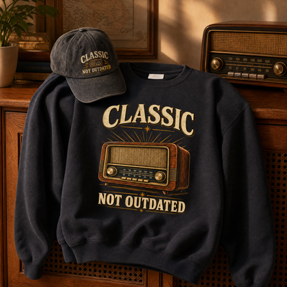 the "Classic. Not Outdated" vintage sweatshirt and cap as the center of the frame draped over a wooden radiator cover, the fabric settling in natural folds, a soft shadow where it meets the wood, a vintage radio sitting level on a table beside it