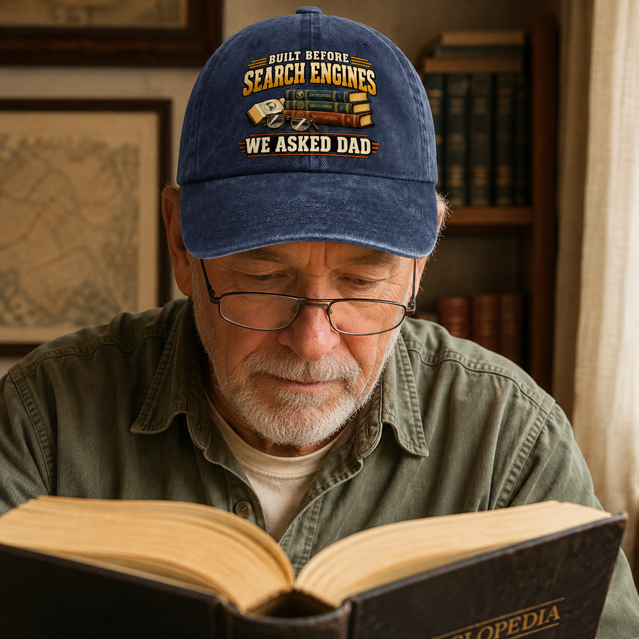 An older man wearing a blue baseball cap with a humorous 'Built Before Search Engines We Asked Dad' graphic, reading a book in a warm, book-filled room.
