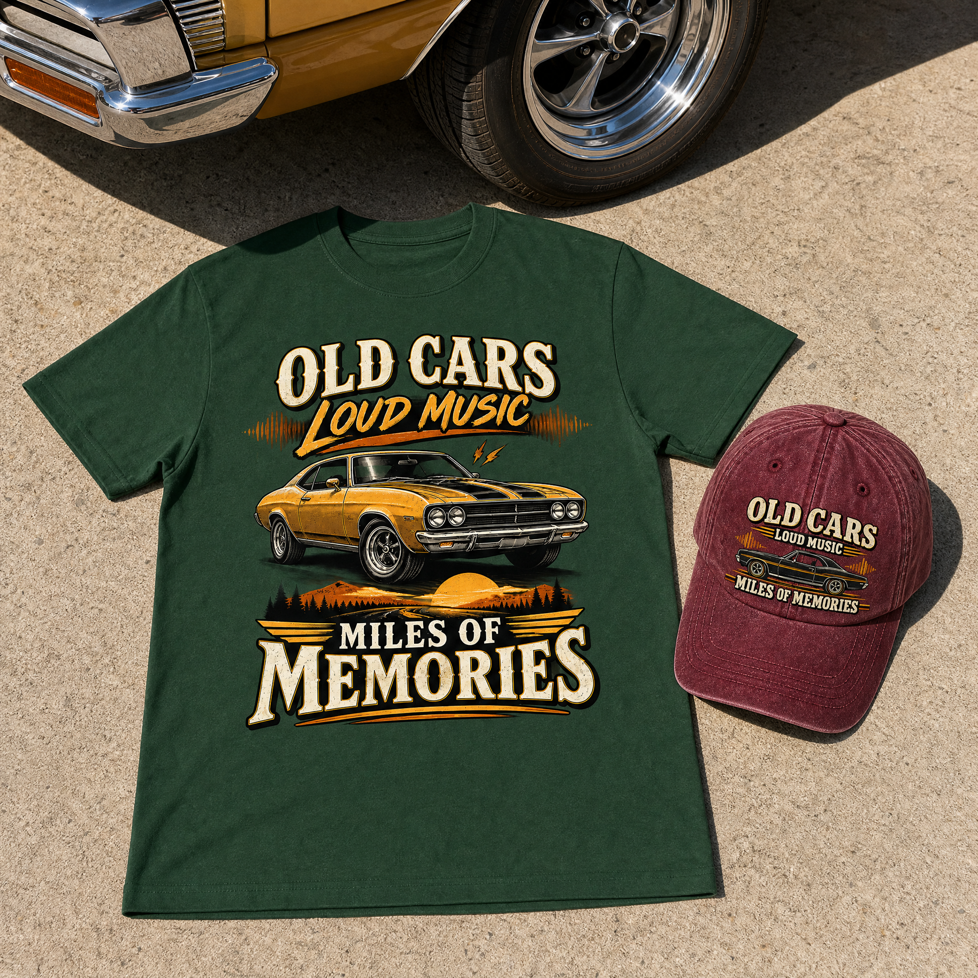 A dark green graphic T-shirt and a maroon baseball cap displayed together on a sandy surface, with part of a classic car visible at the top. The shirt and cap both feature the text 'OLD CARS LOUD MUSIC' and 'MILES OF MEMORIES' around an illustration of a yellow muscle car.
