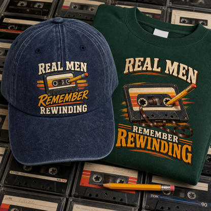 A navy blue baseball cap and a dark green t-shirt, both featuring a retro cassette tape graphic with the text 'REAL MEN REMEMBER REWINDING' in cream and orange lettering. The products are styled on top of vintage cassette tapes and a yellow pencil.