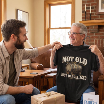 Man holding black T-shirt gift beside wrapped package and fireplace
