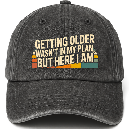 Black vintage washed cap with “Getting Older Wasn’t in My Plan, But Here I Am.” Sunset Fade Reality Cap printed front design