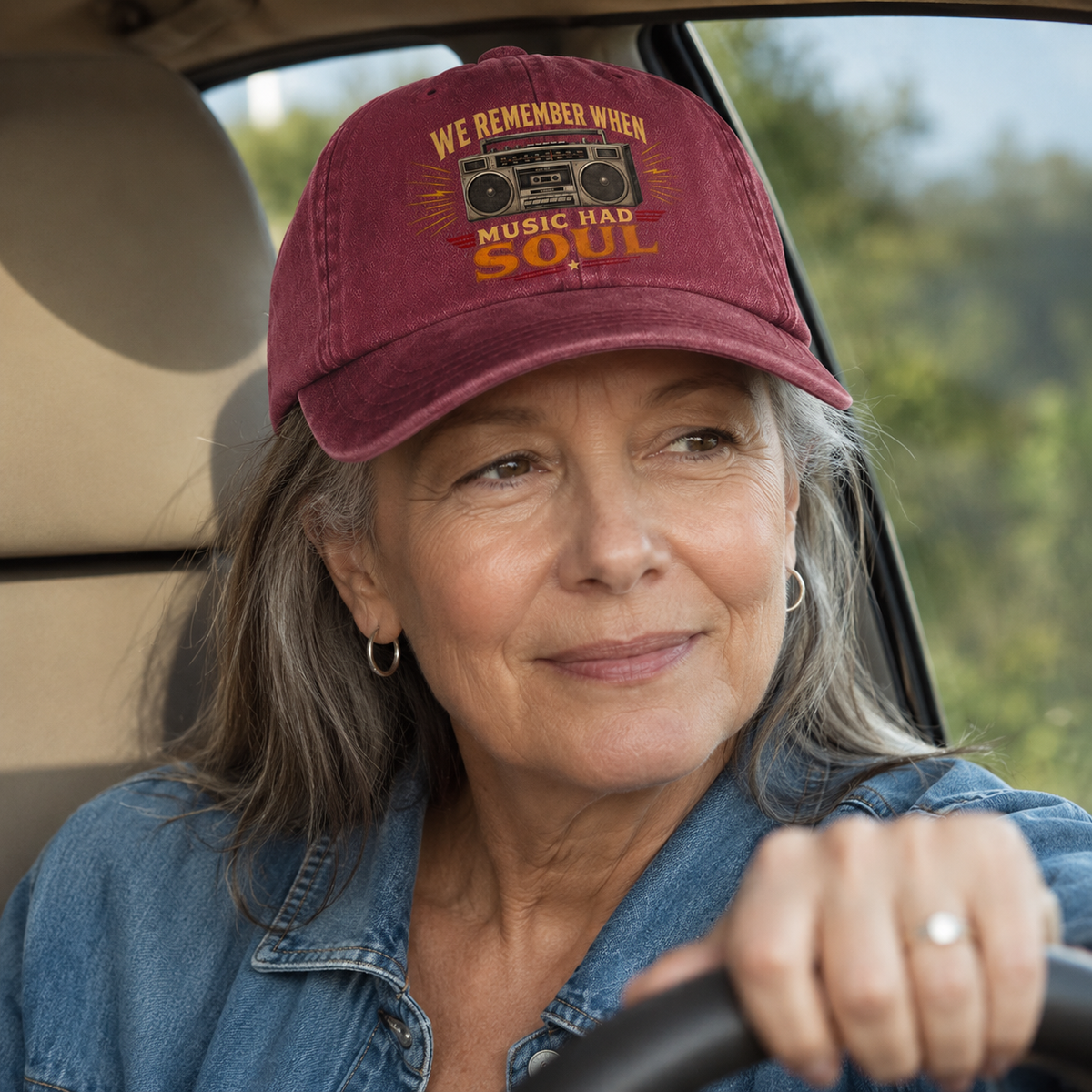 A woman driving a car wearing a maroon baseball cap with a vintage boombox graphic and the text 'WE REMEMBER WHEN MUSIC HAD SOUL'.