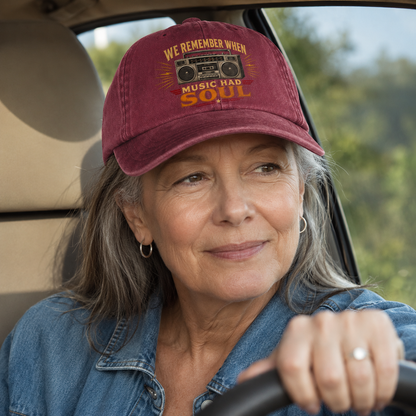 A woman driving a car wearing a maroon baseball cap with a vintage boombox graphic and the text 'WE REMEMBER WHEN MUSIC HAD SOUL'.