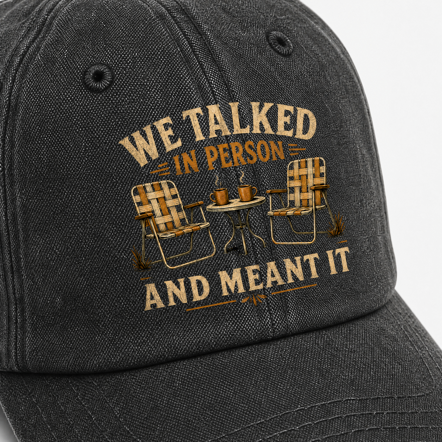 Black vintage washed cap with printed “WE TALKED IN PERSON” slogan and chairs, angled view.