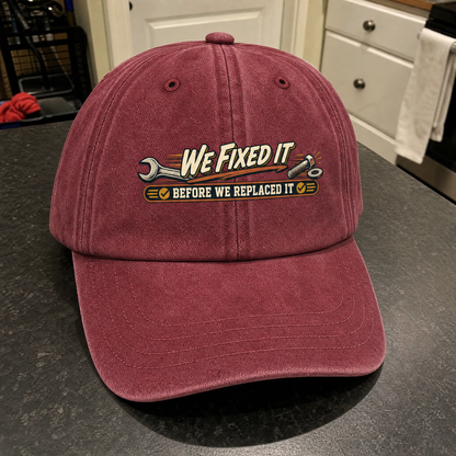 Burgundy vintage washed cap with printed wrench design and We Fixed It slogan, angled view.
