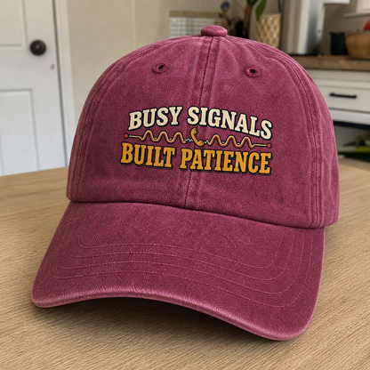 Burgundy vintage washed cap with printed “Busy Signals Built Patience” slogan, angled view.