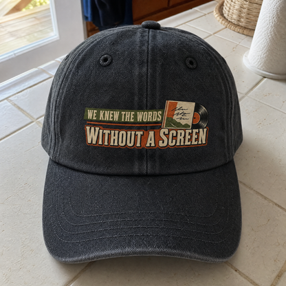 Black vintage washed cap with printed “We Knew the Words Without a Screen” slogan, angled.