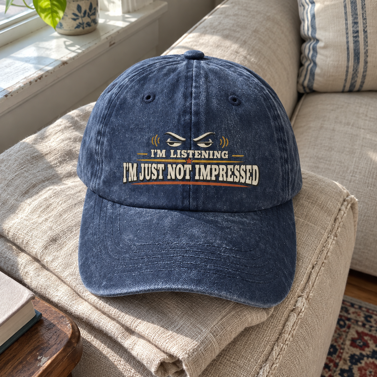 Navy vintage washed cap with printed I'm Listening I'm Just Not Impressed slogan on sofa