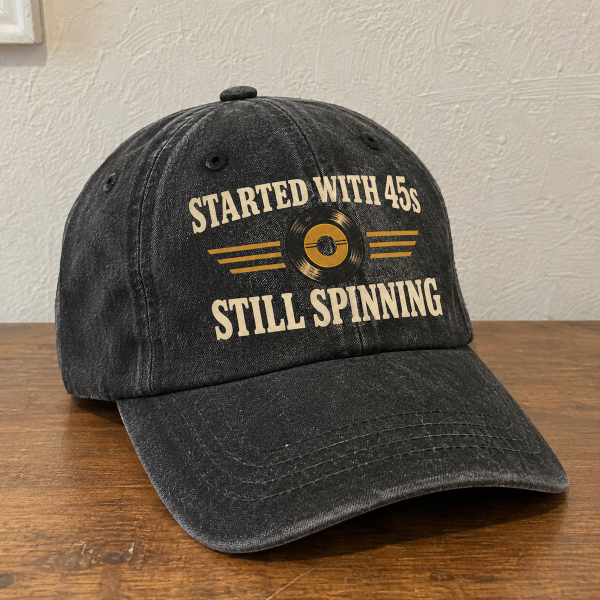Black vintage washed cap with printed “Started With 45s Still Spinning” slogan, angled on wooden table