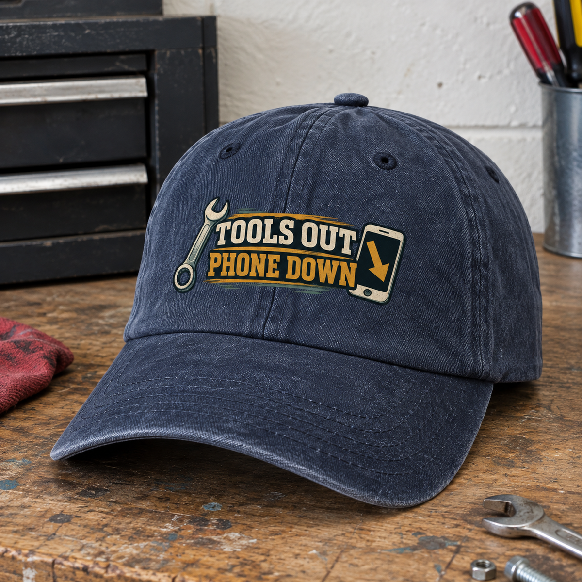 Vintage washed navy cap with Tools Out Phone Down printed design, shown at an angle on workbench