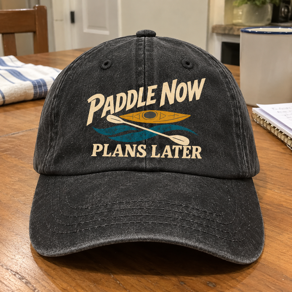 Black vintage washed cap with printed Paddle Now Plans Later kayak design, front angle