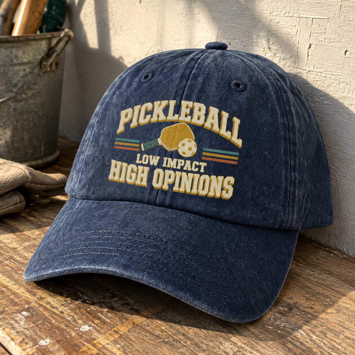 vintage washed cap with printed Pickleball Low Impact High Opinions slogan, angled on rustic table.