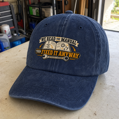 Navy vintage washed cap with printed “We Read The Manual Then Fixed It Anyway” design, angled view