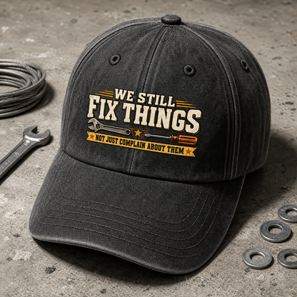 Black vintage washed cap with printed “We Still Fix Things” slogan, angled view.