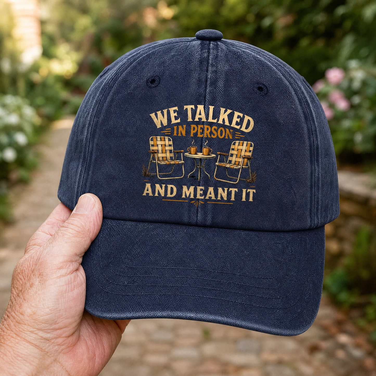 Navy vintage washed cap with “WE TALKED IN PERSON AND MEANT IT” printed design, handheld.