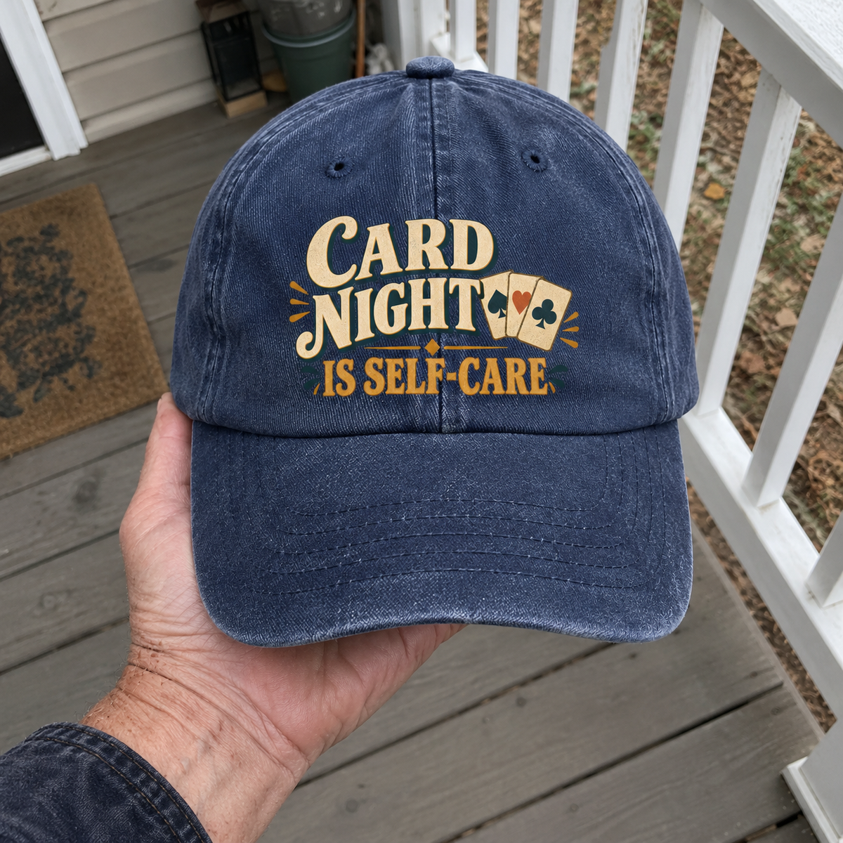 Blue vintage washed cap with printed Card Night Is Self-Care slogan, held by hand outdoors.