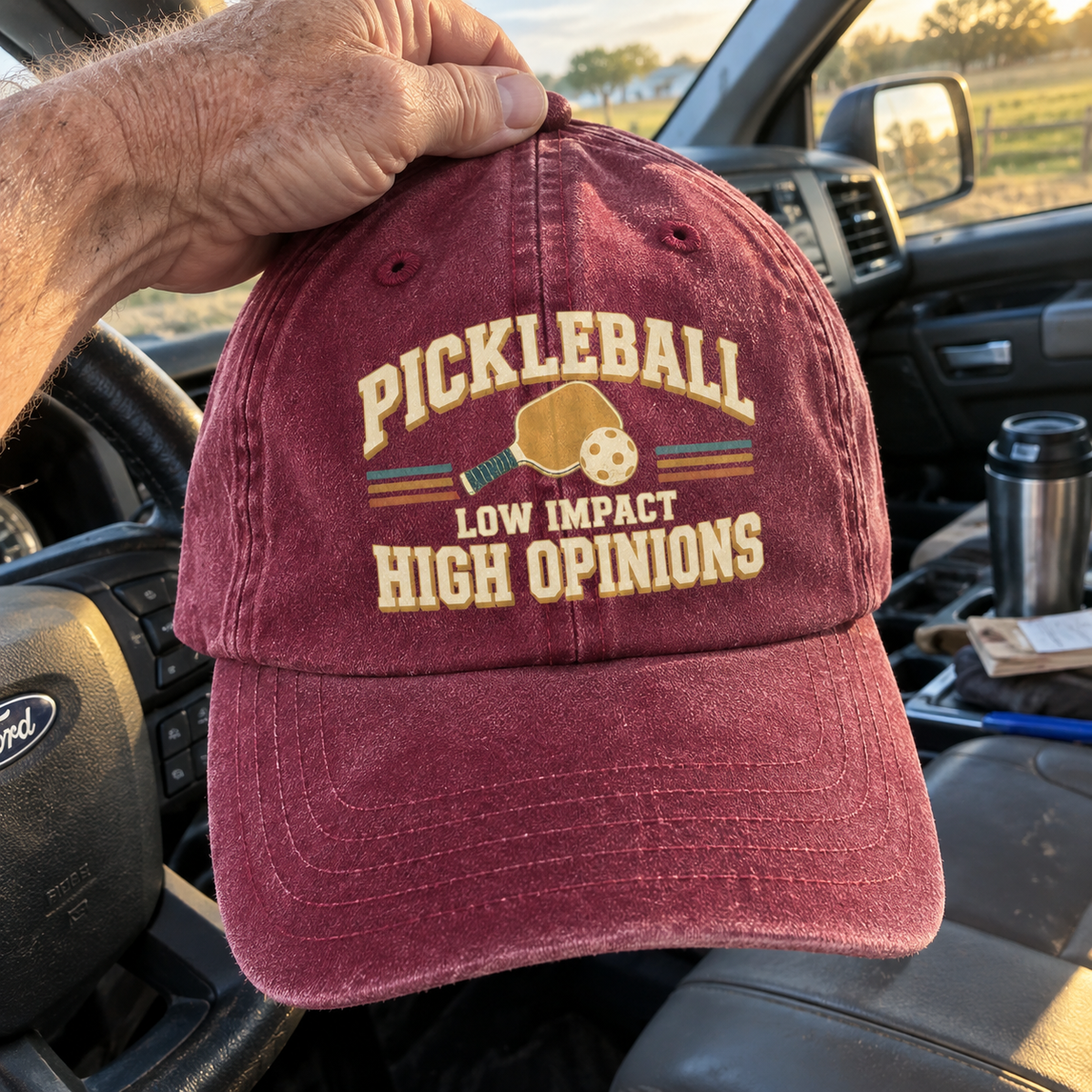 Burgundy vintage washed cap with printed pickleball slogan, handheld inside a vehicle