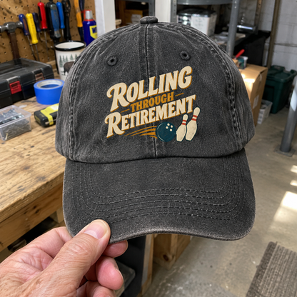 Black vintage washed cap with printed Rolling Through Retirement slogan and bowling design, handheld front view