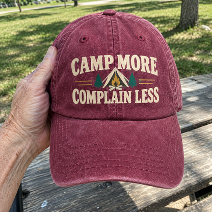 Maroon vintage washed cap with printed Camp More. Complain Less slogan, handheld outdoors