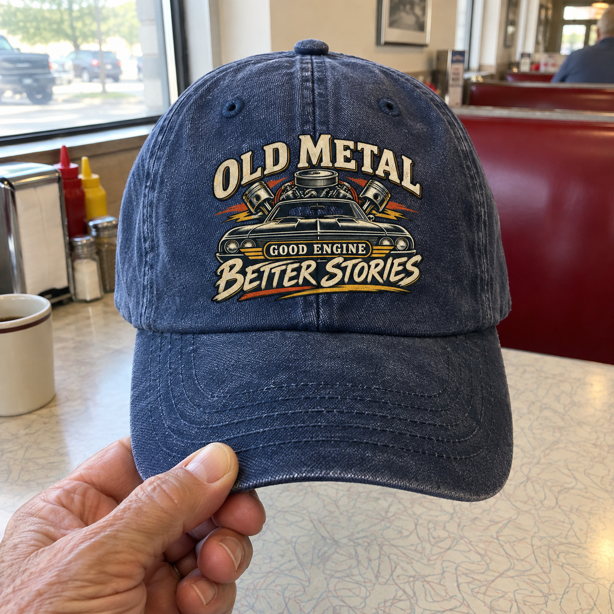 Blue vintage washed cap with printed Old Metal Good Engine Better Stories design, handheld view.