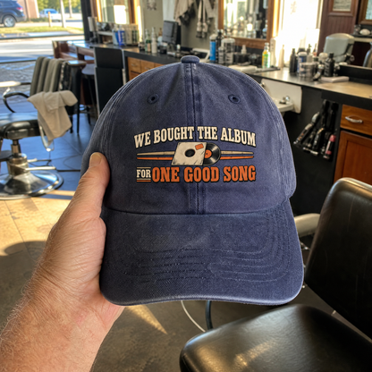 Blue vintage washed cap with “We Bought The Album For One Good Song” slogan, handheld.