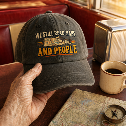 Vintage washed cap printed with “We Still Read Maps And People,” handheld view