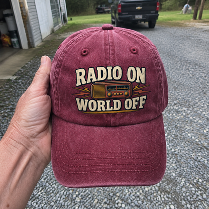 Maroon vintage washed cap with printed Radio On World Off slogan held outdoors