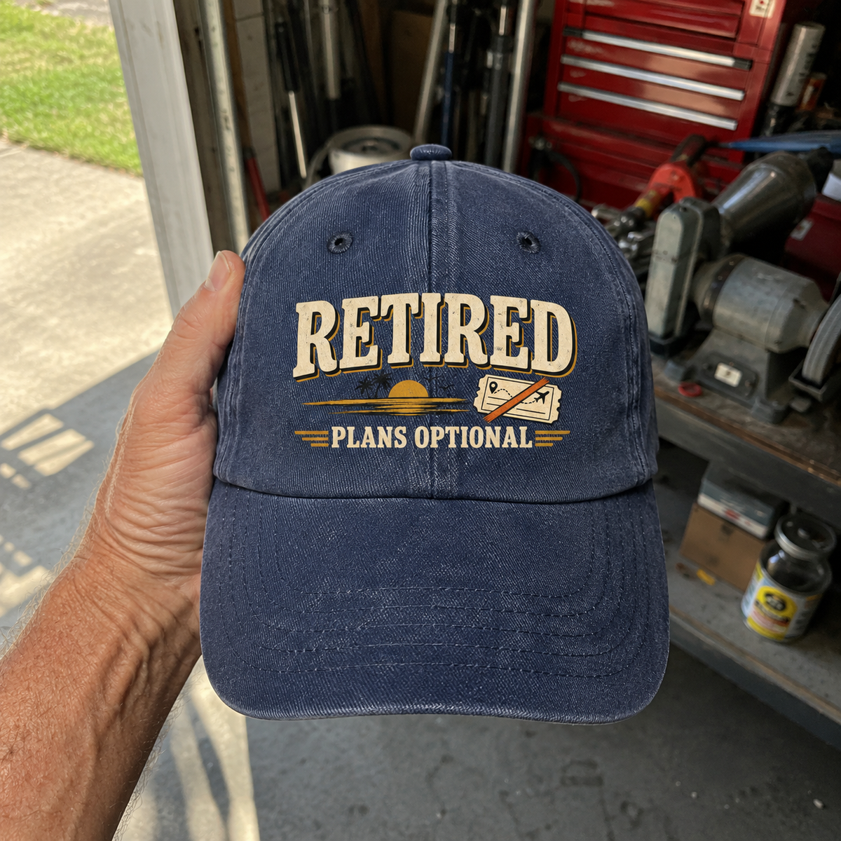 Blue vintage washed cap with printed “Retired Plans Optional” slogan, handheld front view.