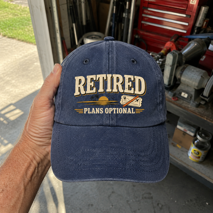 Blue vintage washed cap with printed “Retired Plans Optional” slogan, handheld front view.