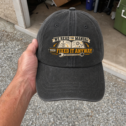 Vintage washed cap with printed “We Read the Manual Then Fixed It Anyway” design, handheld