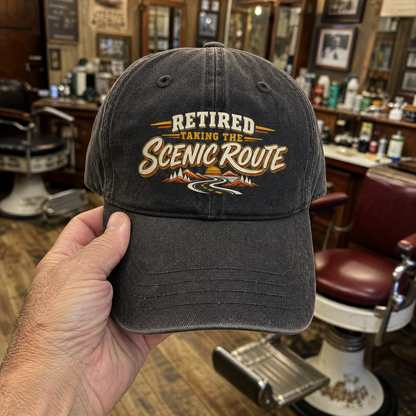 Black vintage washed cap printed with “Retired. Taking The Scenic Route” and mountain road design.