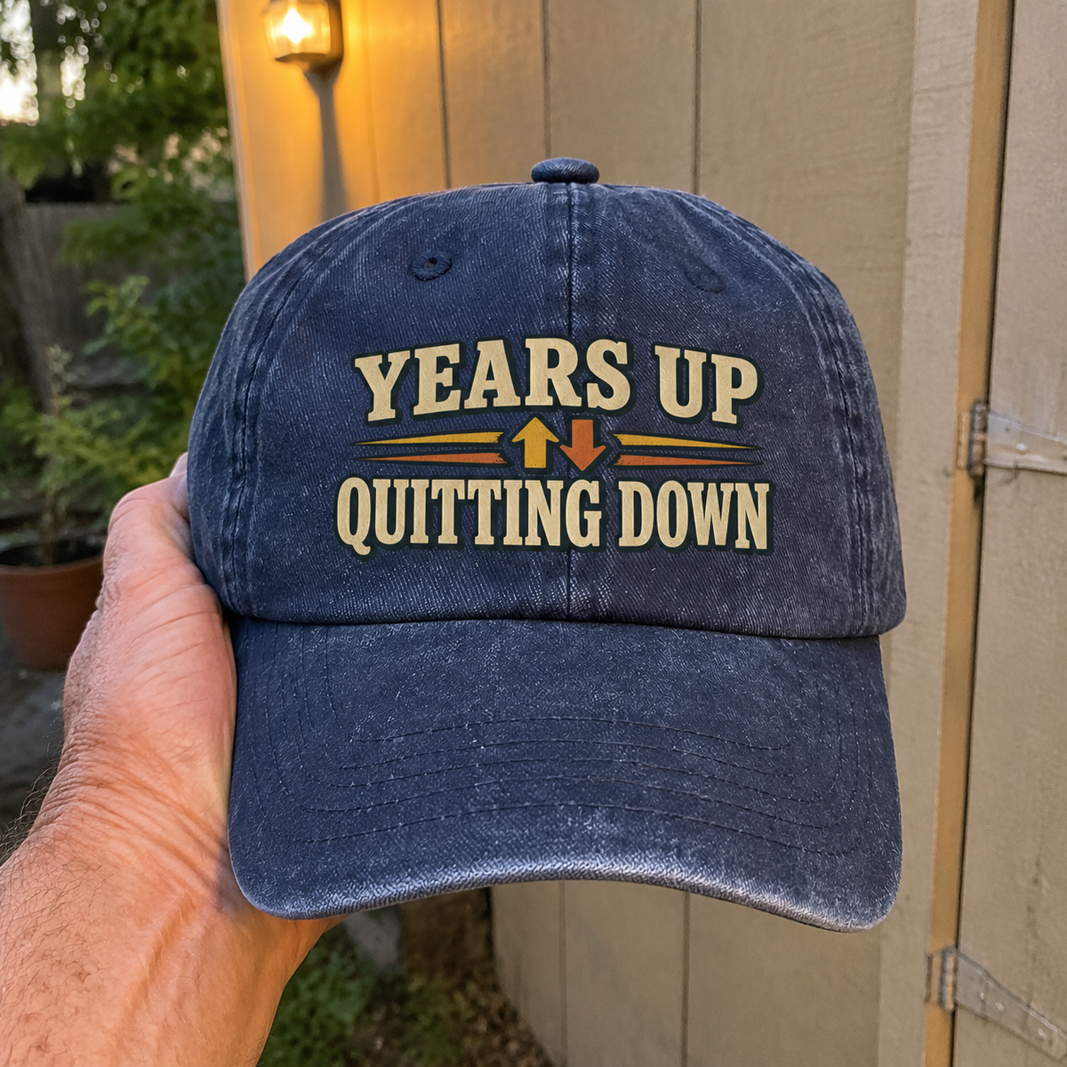 Blue vintage washed cap with printed Years Up Quitting Down slogan held by hand