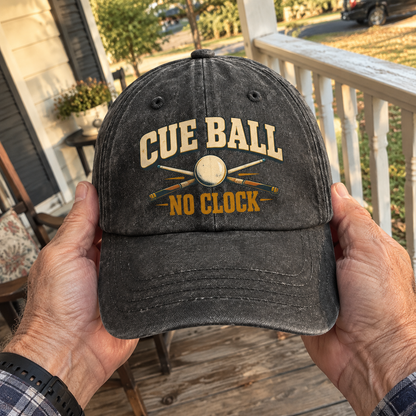Black vintage washed cap with printed Cue Ball No Clock billiards design, handheld front view on a porch.