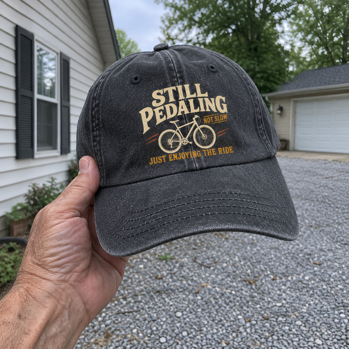 Handheld black vintage washed cap with printed Still Pedaling Not Slow bicycle ride design