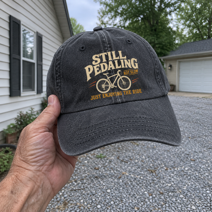 Handheld black vintage washed cap with printed Still Pedaling Not Slow bicycle ride design
