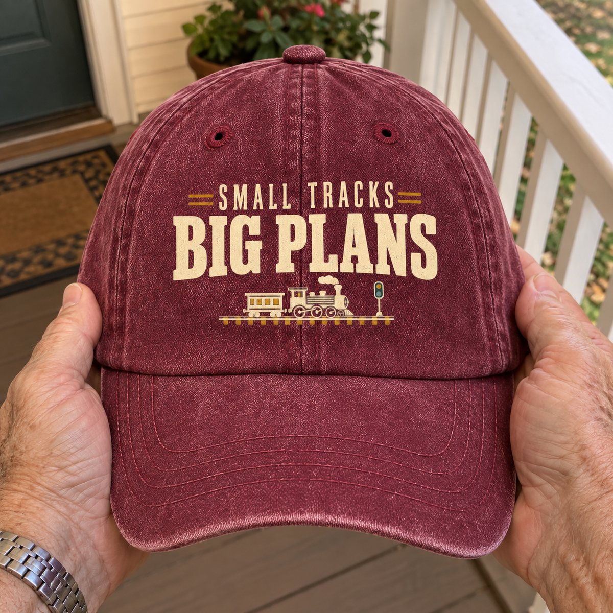 Burgundy vintage washed cap with printed Small Tracks Big Plans slogan, handheld front view