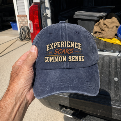 Handheld navy vintage washed cap with Experience Scars Common Sense printed design
