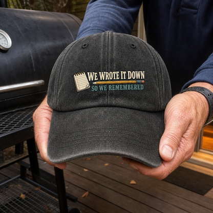 Black vintage washed cap with printed “We Wrote It Down So We Remembered” held by hands