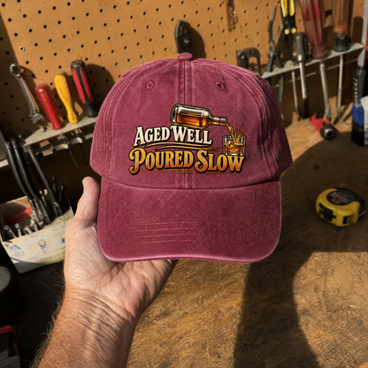 Burgundy vintage washed cap featuring printed “Aged Well. Poured Slow” slogan, handheld view.