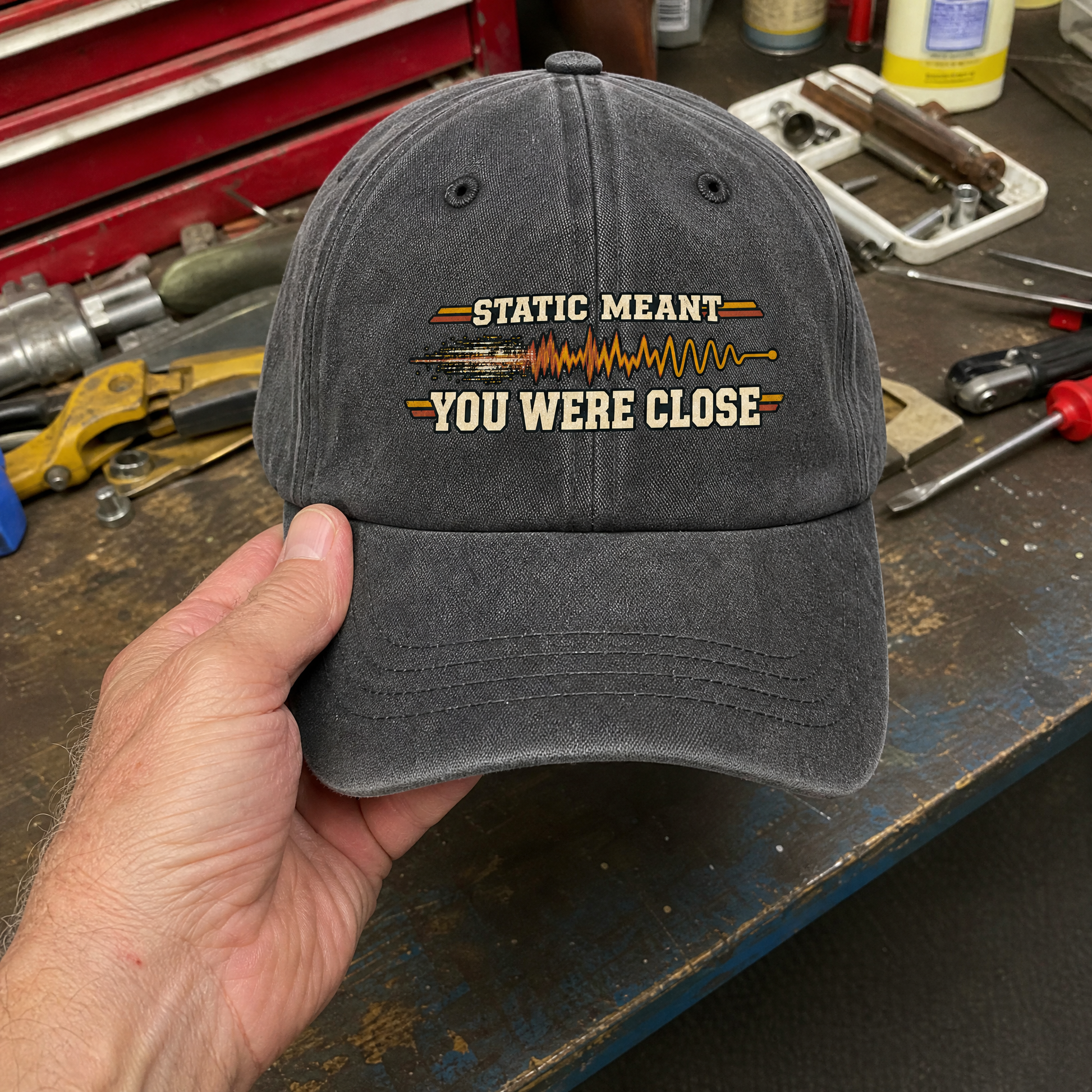 Gray vintage washed cap with printed Static Meant You Were Close slogan held by hand