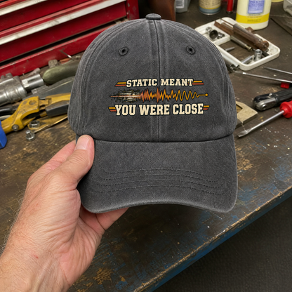 Gray vintage washed cap with printed Static Meant You Were Close slogan held by hand