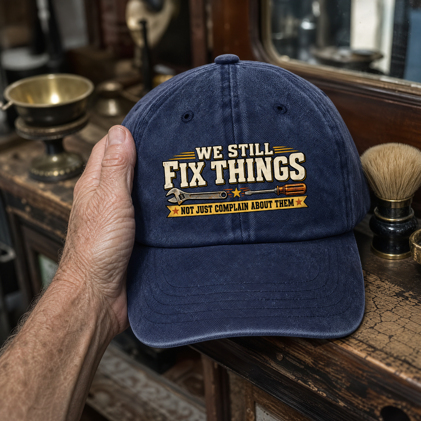 Blue vintage washed cap held by hand, printed with We Still Fix Things slogan.