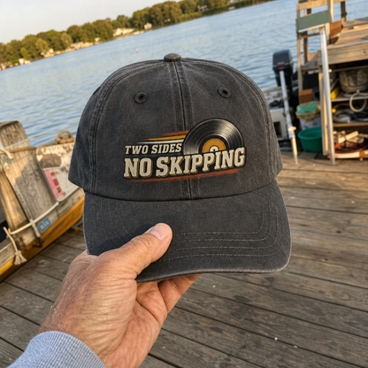 Vintage washed cap with Two Sides. No Skipping printed design, handheld near lakeside dock.